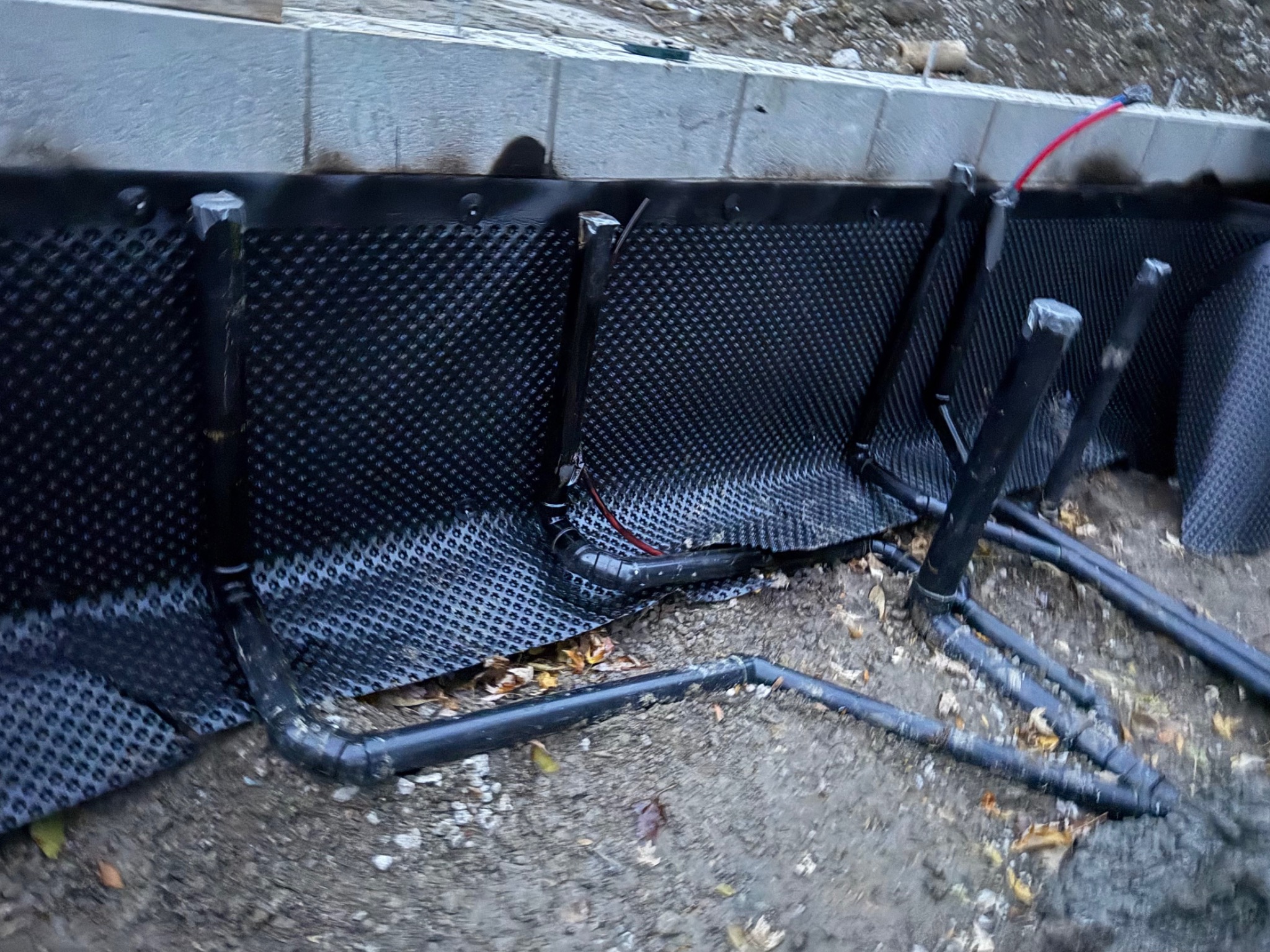 Dimpled drainage membrane installed at foundation walls with coordinated underground services